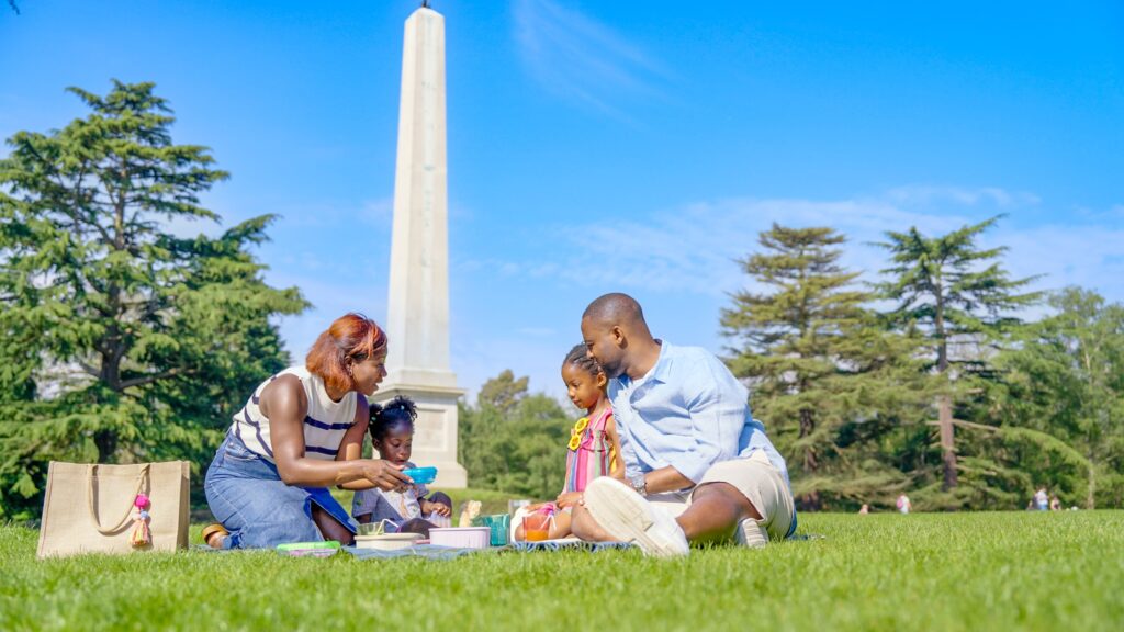 Family having a picnic on the grass sitting on a blanket with a picnic basket.