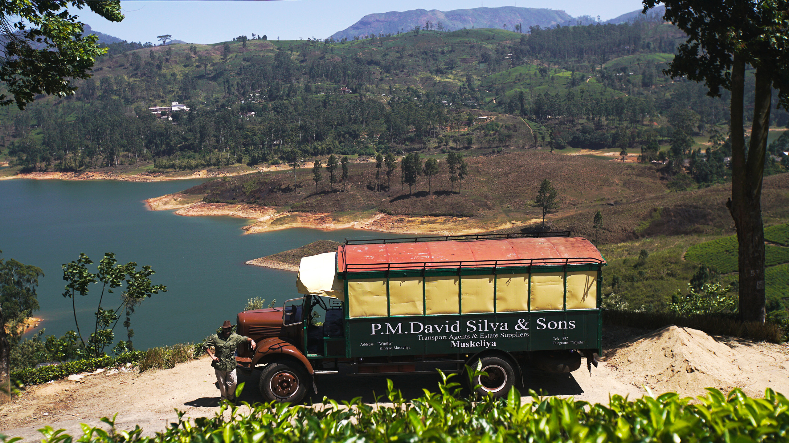 A lorry parked on a path with a green mountainous landscape behind.