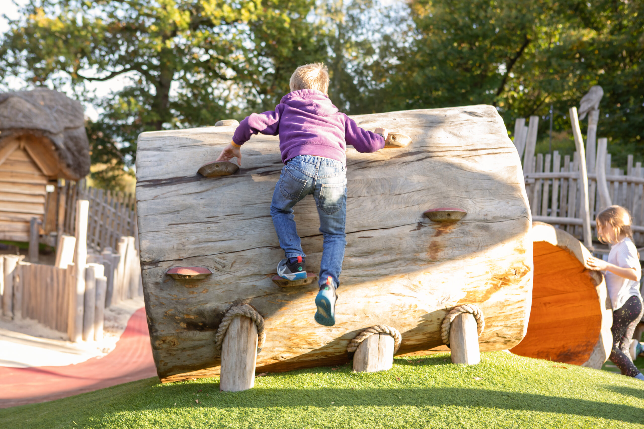 Young child climbing a hollow wooden log at Adventure Play.