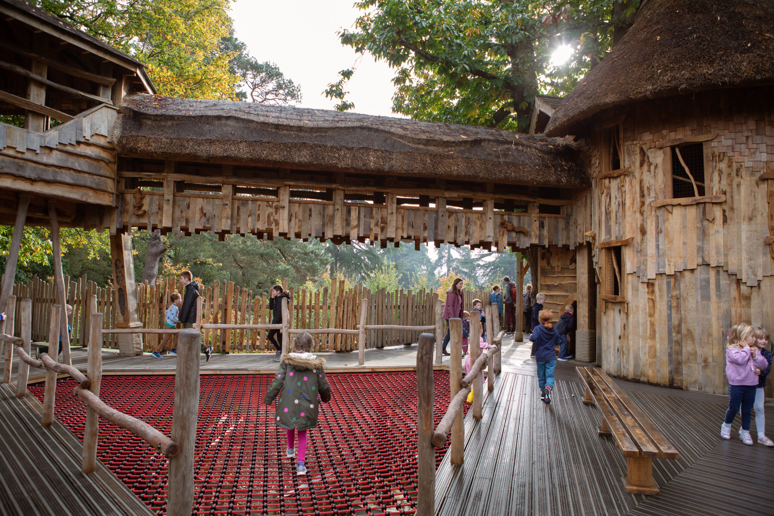 Young child walking across a red net floor surrounded by other children on a wooden walkway.