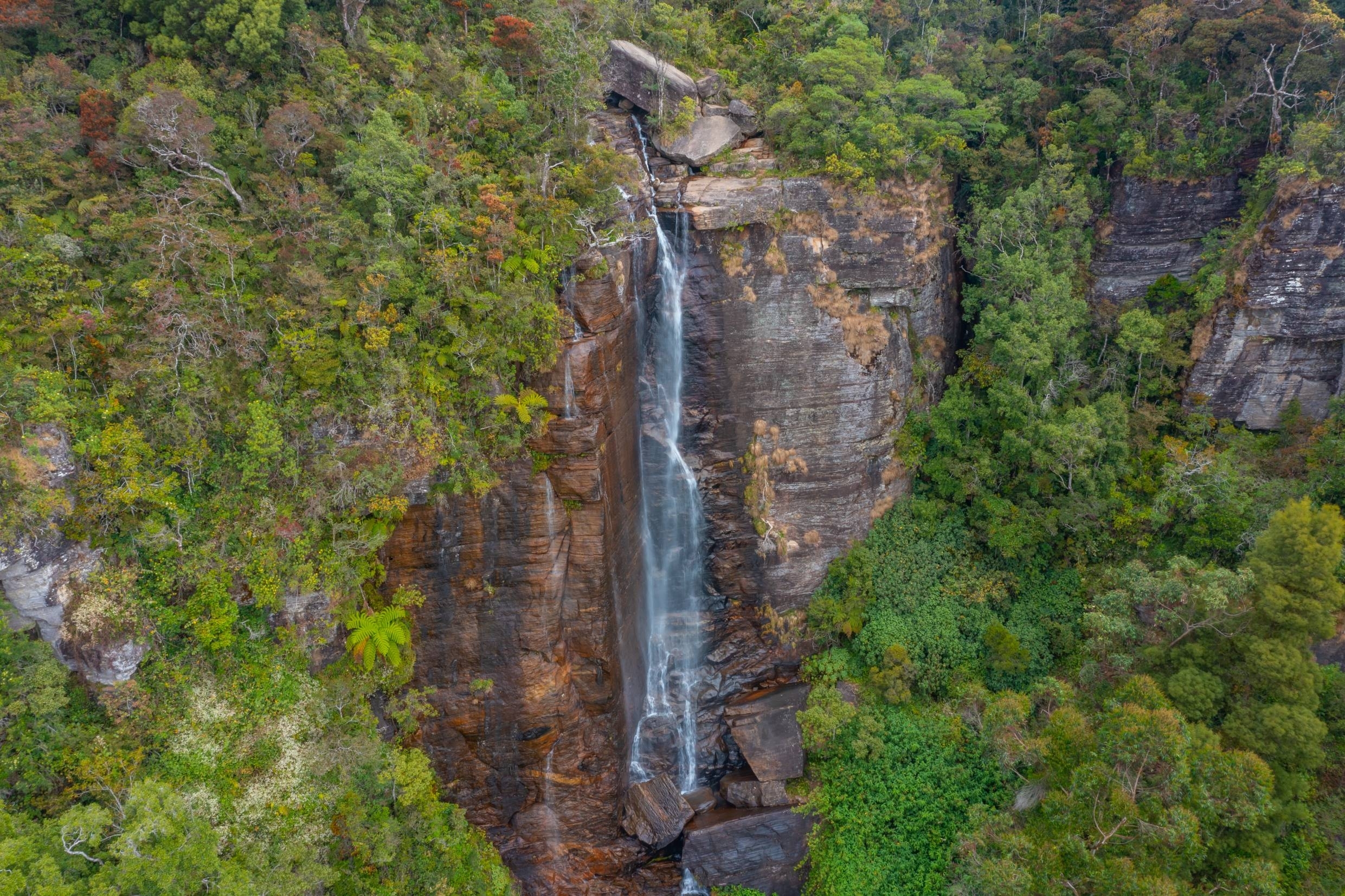 An aerial photo of a waterfall beside trees.