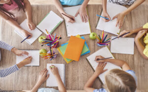 An aerial view of children at a table, writing on paper.