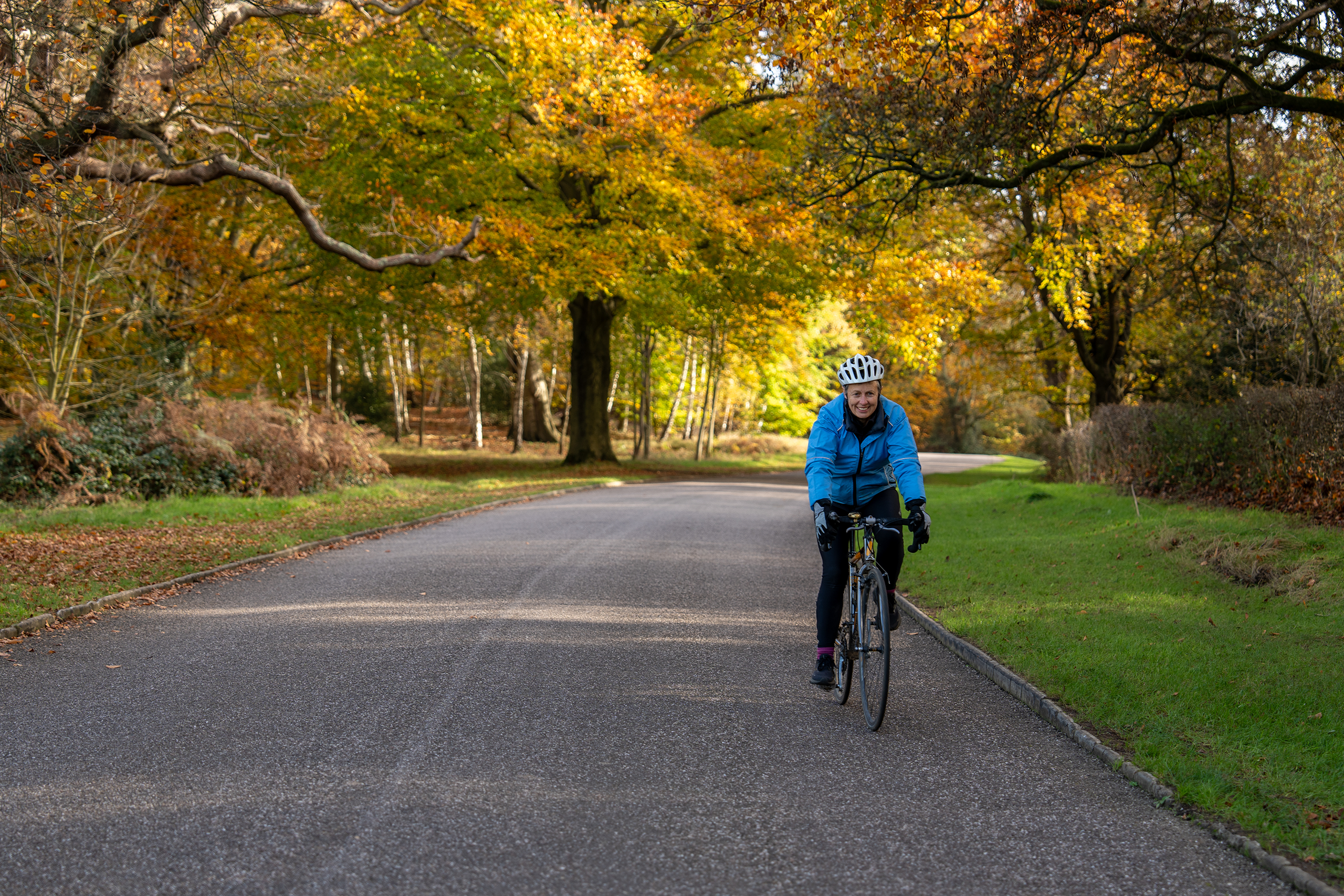 Two adults on their bikes. Wearing helmets, cycling on a path.