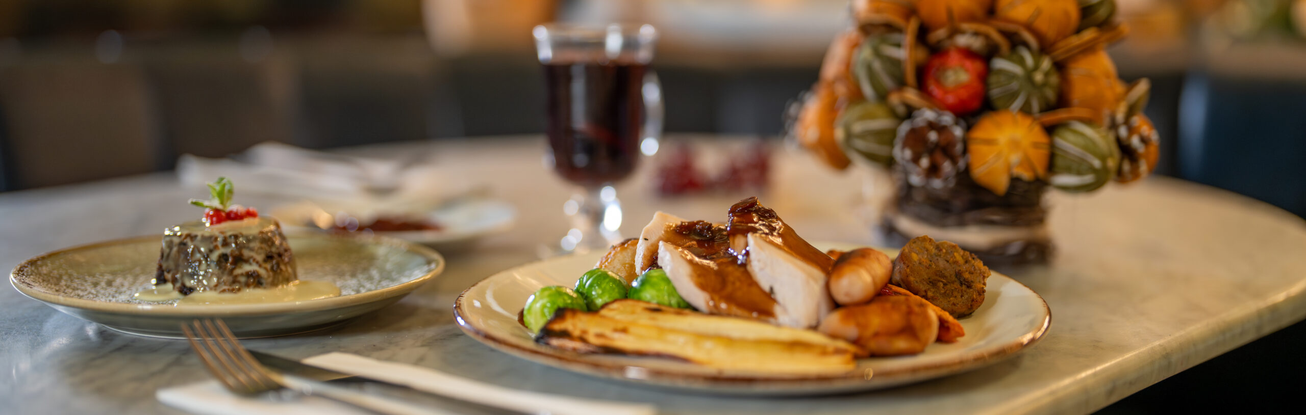 A table laid with a Christmas dinner, mulled wine, Christmas pudding and Christmas tree decoration