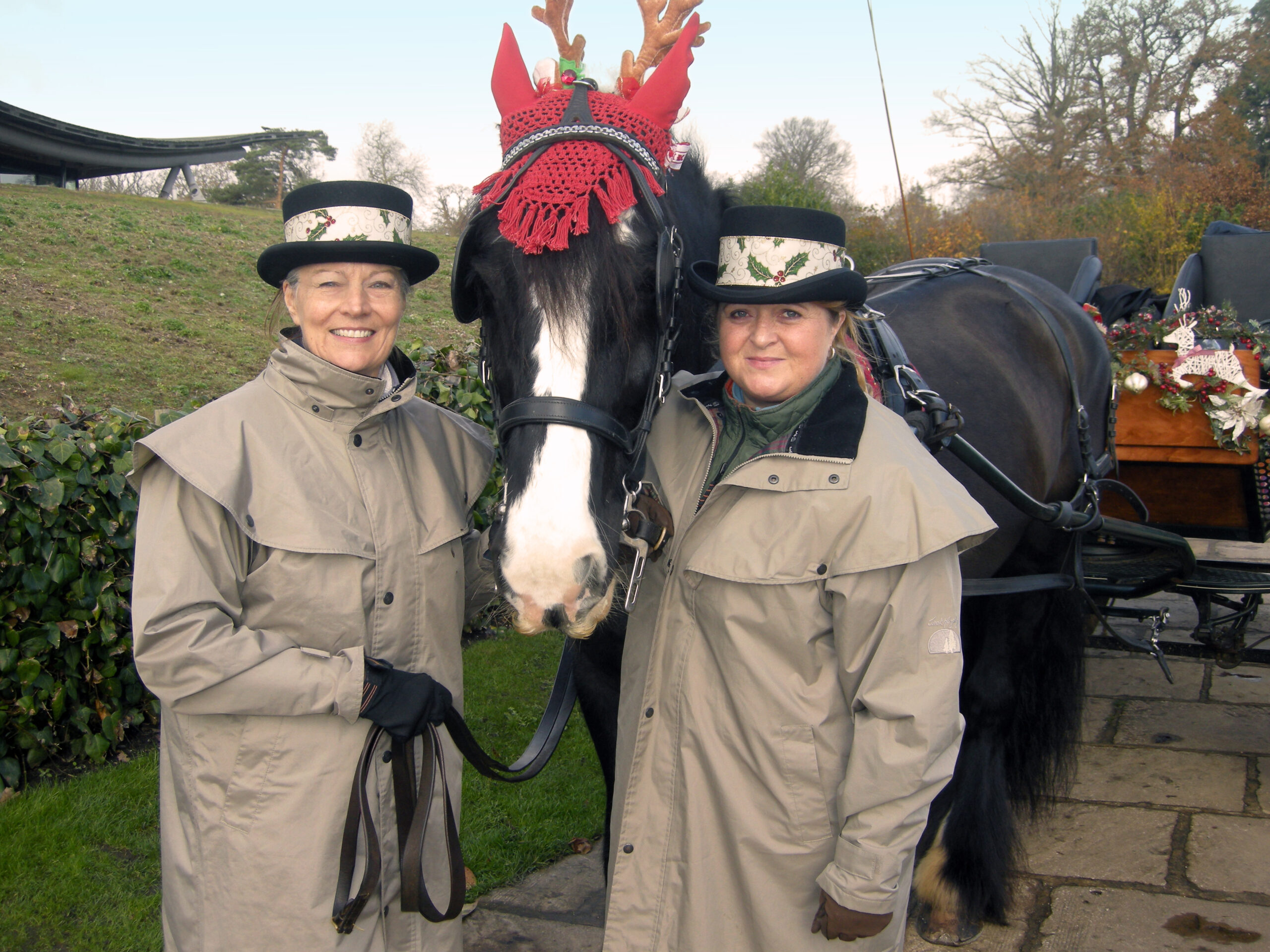 Two adults standing with a horse wearing a Christmas themed head dress.