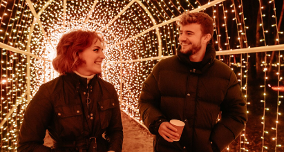 Two people walking through a tunnel lit up by fairy lights.